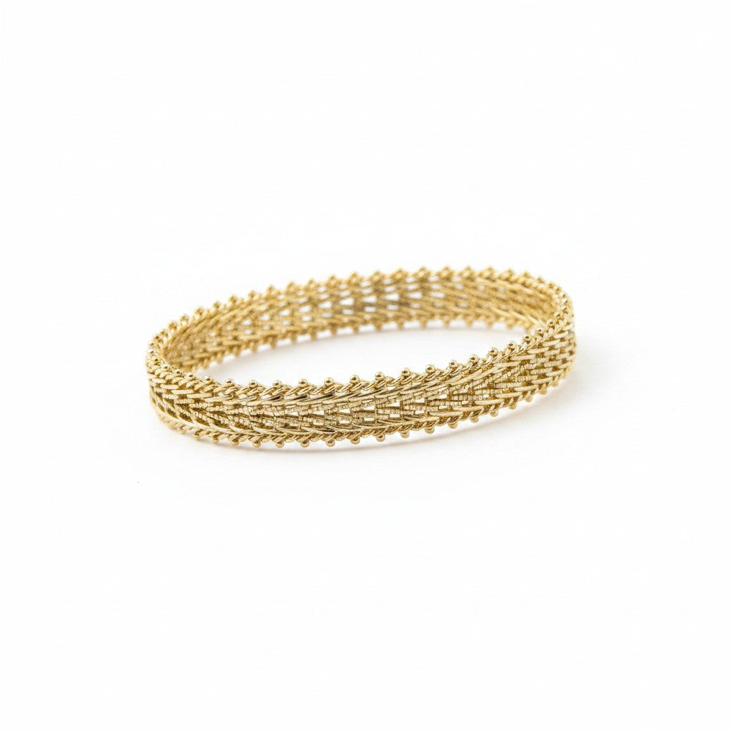 ANIBA JEWELS gold gourmette bracelet with intricate woven design and beaded edges, displayed on a cream stand.